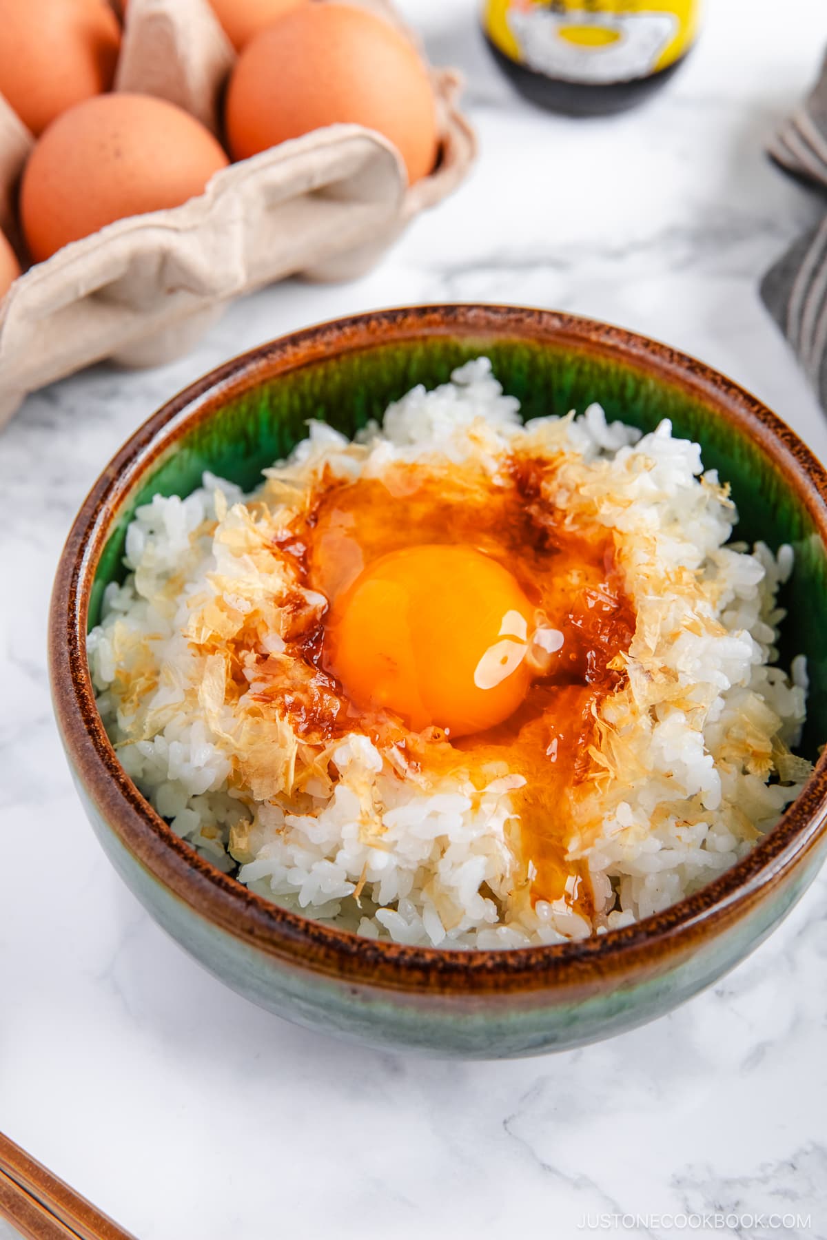 A bowl containing steamed rice, raw egg, sprinkled katsuobushi, and a drizzle of soy sauce.