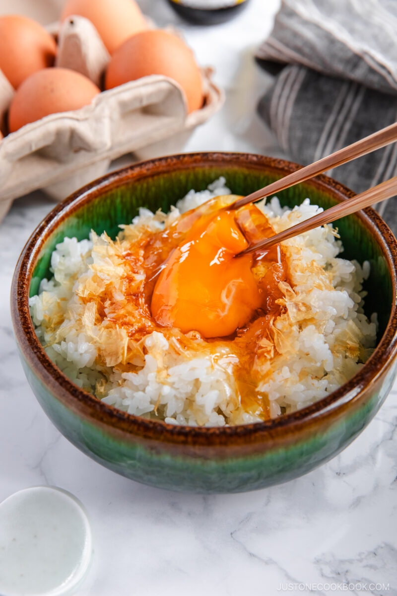 A bowl containing steamed rice, raw egg, sprinkled katsuobushi, and a drizzle of soy sauce.