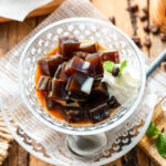 Glass bowls containing Coffee Jelly, drizzled with cream and topped with fresh whipped cream.