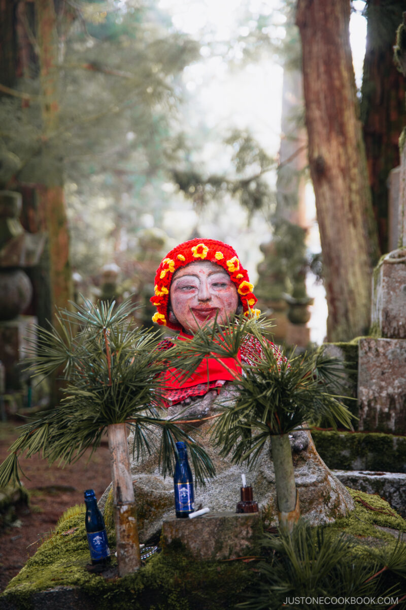 Stone buddha statue with red hat, bib, and makeup