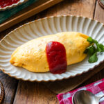 An oval plate containing Omurice (Japanese Omelette Rice) drizzled with Japanese ketchup.