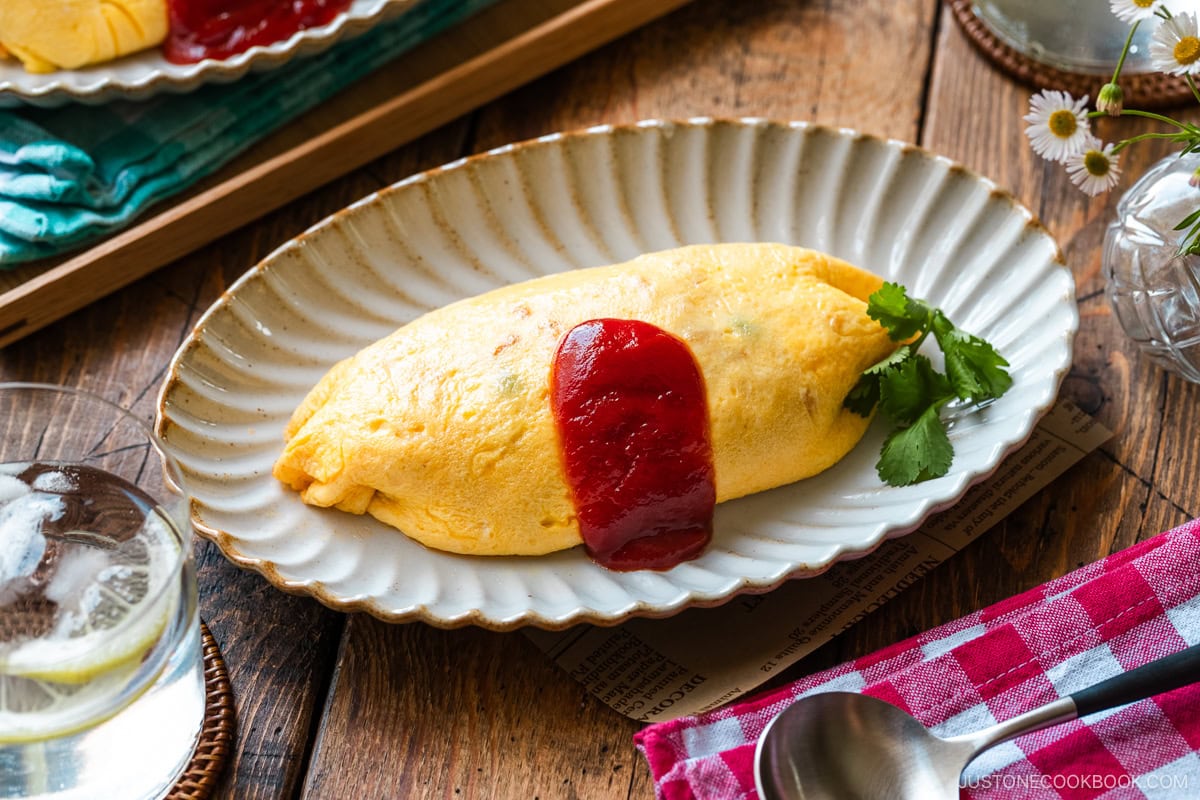 An oval plate containing Omurice (Japanese Omelette Rice) drizzled with Japanese ketchup.