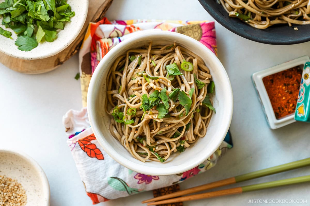 A white bowl containing Soba Noodle Salad topped with sesame seeds and chopped cilantro and green onions.