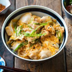 A Japanese ceramic bowl containing Oyakodon, a chicken and egg rice bowl dish garnish with green onion.