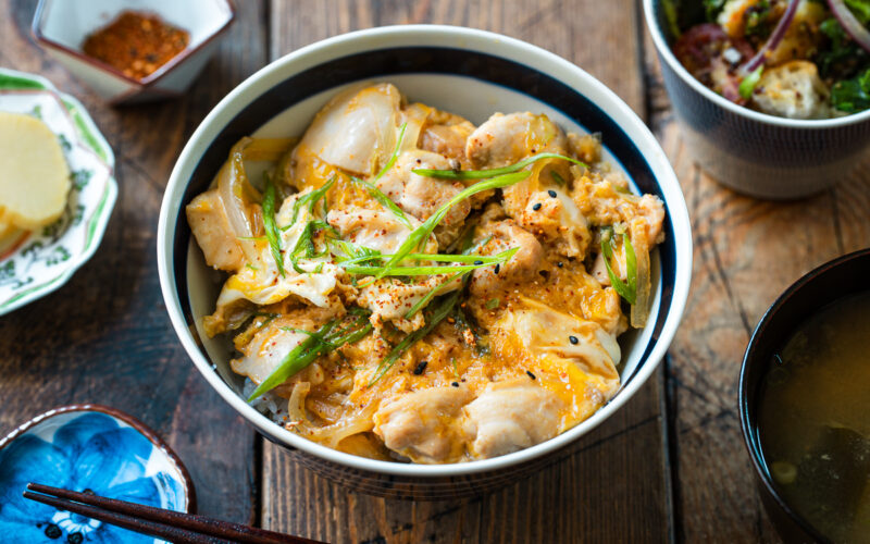 A Japanese ceramic bowl containing Oyakodon, a chicken and egg rice bowl dish garnish with green onion.