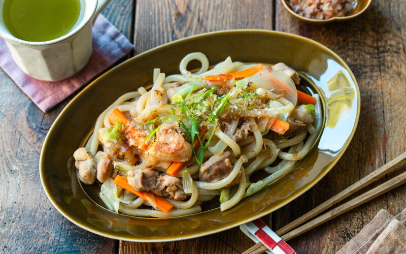 An olive colored oval plate containing Yaki Udon, Japanese stir-fried udon noodles with chicken and vegetables.