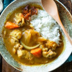 A round plate containing Japanese chicken curry over steamed rice, garnished with fukujinzuke pickles.