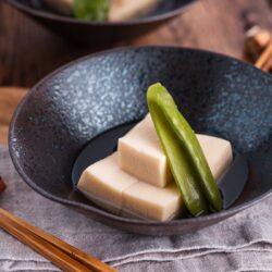 Simmered koyadofu with snow peas in a black ceramic bowl.