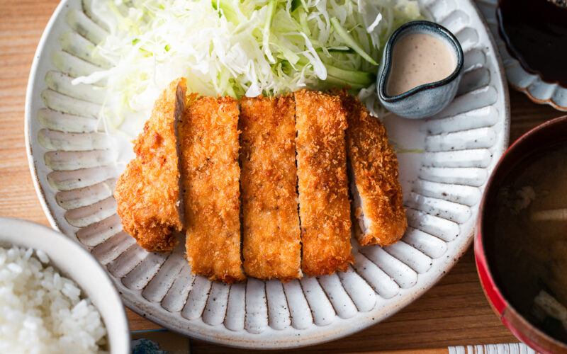 A Japanese ceramic plate containing Tonkatsu (pork cutlet) and shredded cabbage salad.