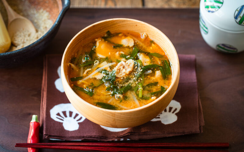 A light wooden bowl containing Spicy Pork and Bean Sprout Miso Soup sprinkled with ground sesame seeds.