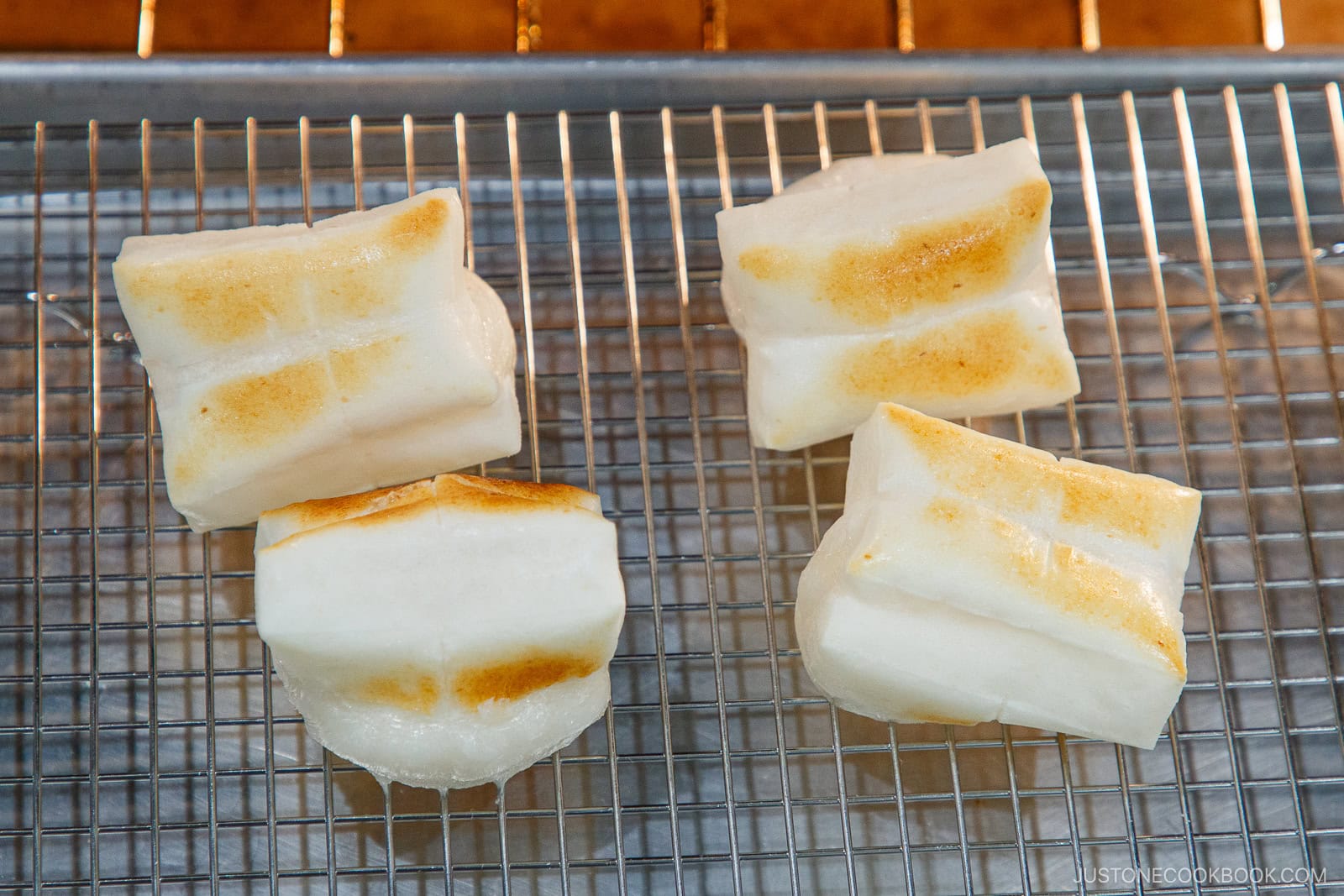 Golden-brown grilled mochi rice cakes resting on a wire cooling rack, showcasing their crispy exterior perfect for Japanese dessert recipes or snacks.