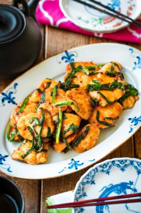 An oval plate containing Chicken Stir-fry with Garlic Chives served on the table along with tea pot and small plates.