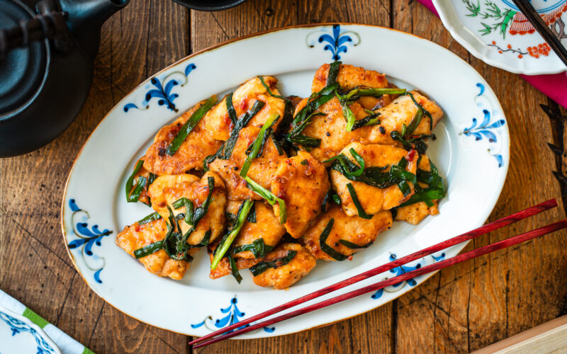 An oval plate containing Chicken Stir-fry with Garlic Chives served on the table along with tea pot and small plates.