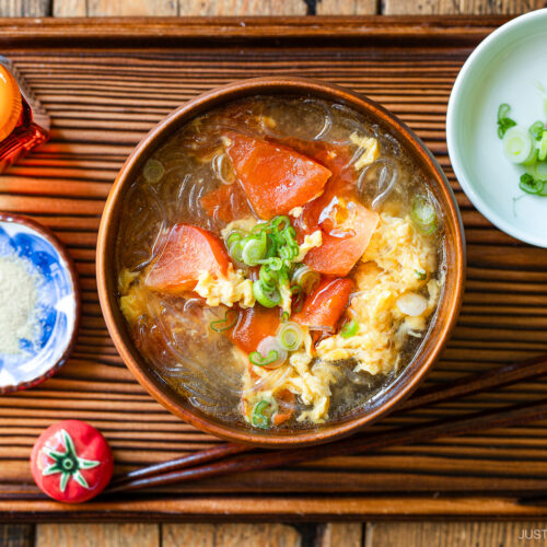 A wooden bowl containing tomato egg vermicelli soup garnished with green onion.