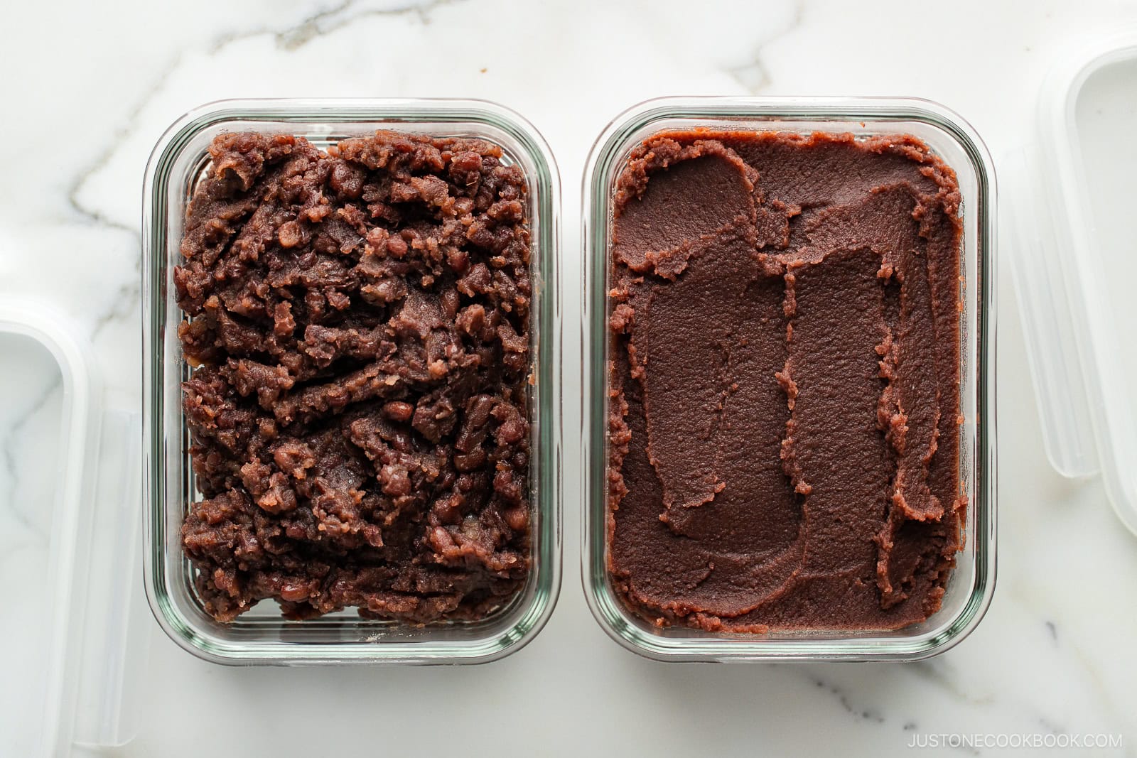 Two glass containers on a white marble surface, one filled with chunky red bean paste and the other with smooth red bean paste. Both pastes are deep brownish-red in color.