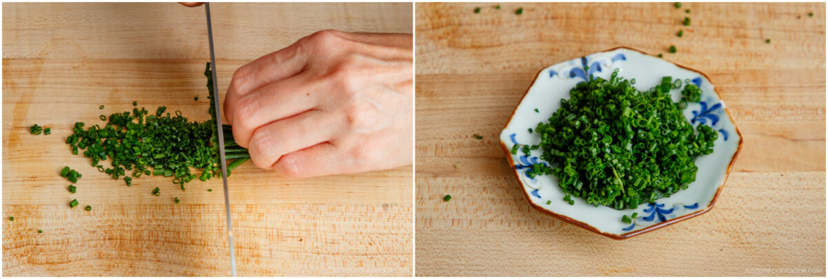 A hand finely chops chives on a wooden cutting board. Next to it, a small decorative plate holds a pile of the freshly chopped chives.