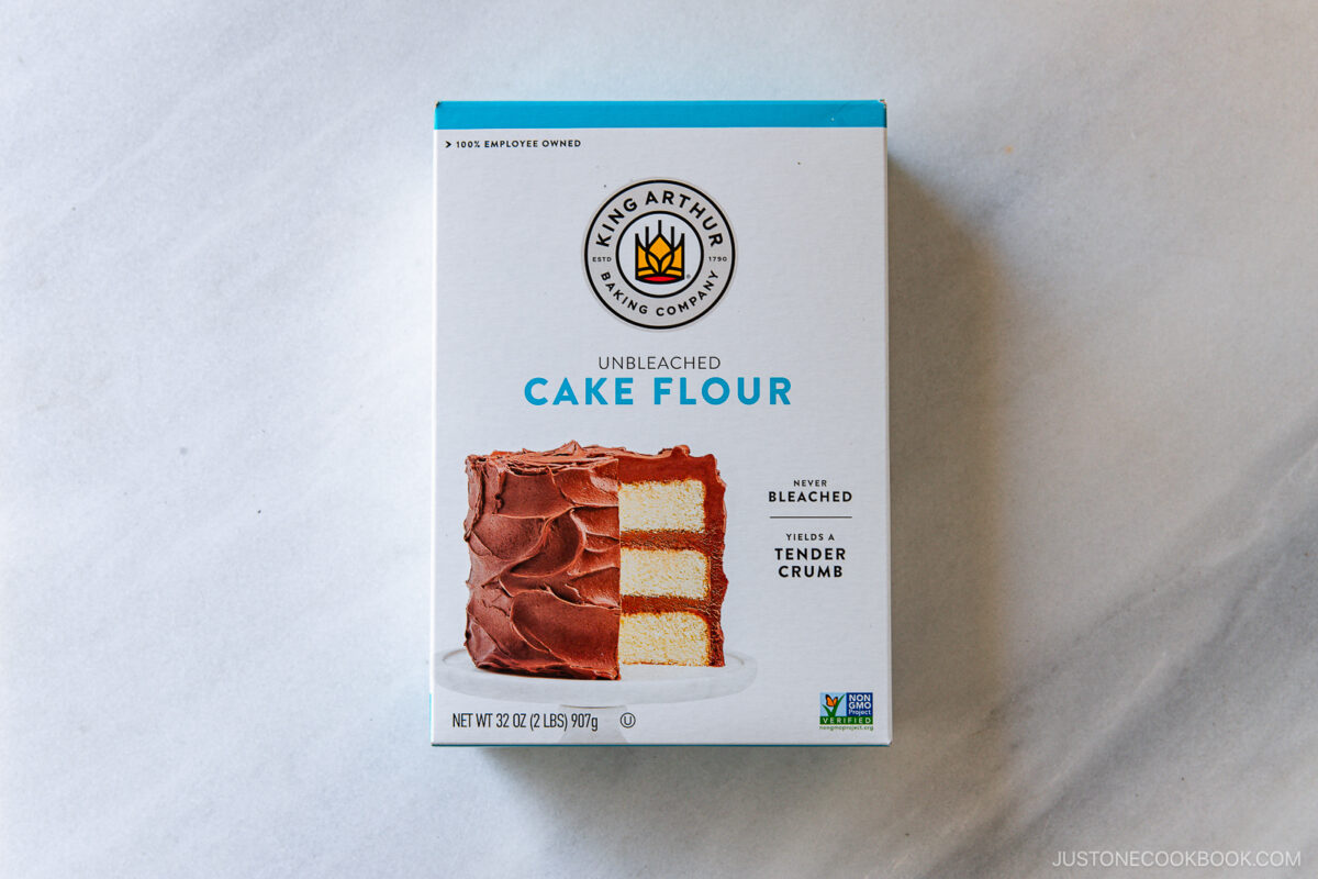 A box of King Arthur Baking Company Unbleached Cake Flour featuring an image of a frosted layer cake on the front, placed on a light gray surface.