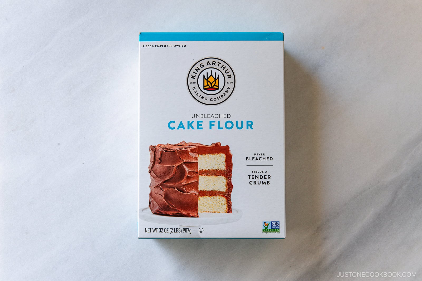 A box of King Arthur Baking Company Unbleached Cake Flour featuring an image of a frosted layer cake on the front, placed on a light gray surface.
