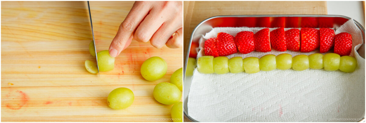 A hand slices green grapes on a wooden cutting board; next to it, halved strawberries and grapes are neatly lined up on a paper towel in a metal tray.