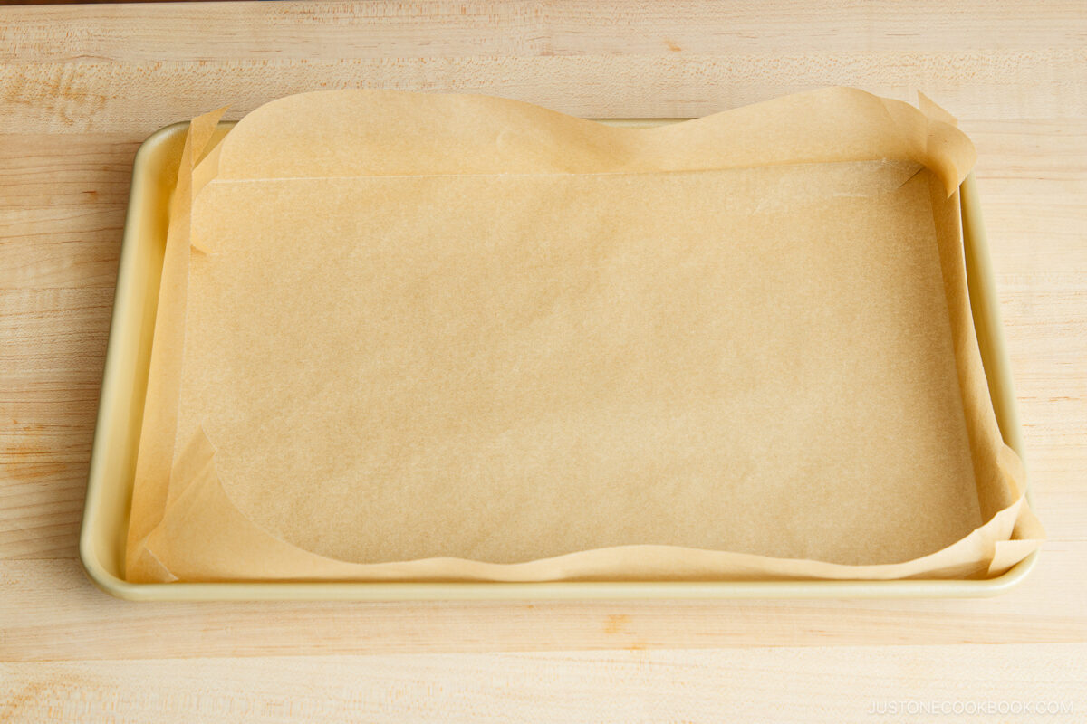 A rectangular baking tray lined with parchment paper sits on a light wooden surface, ready for use.