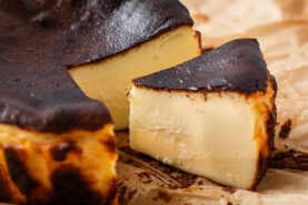 A close-up of a sliced Basque burnt cheesecake on parchment paper, showing its creamy interior and dark, caramelized top.