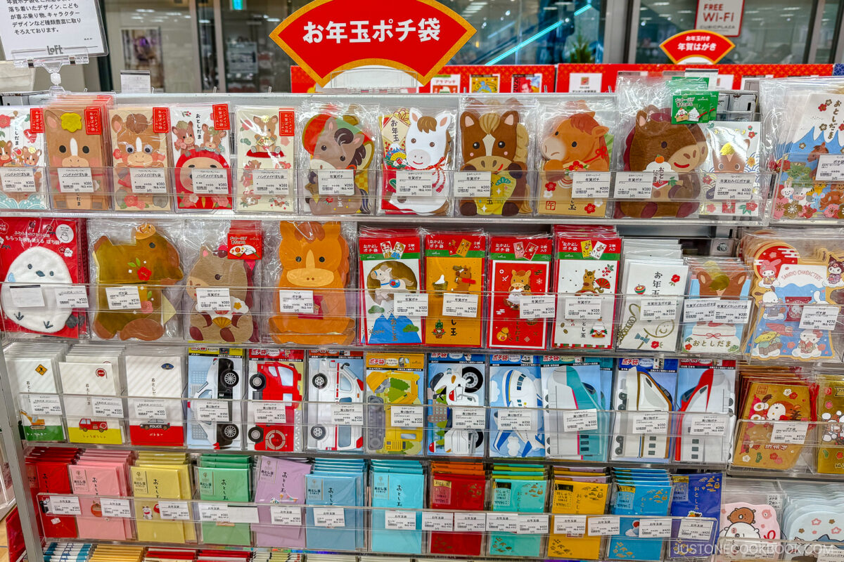 A store display features colorful Japanese envelopes, many with animal designs like rabbits, bears, and cows, as well as festive patterns. The display is neat, and there are Japanese signs and labels throughout.