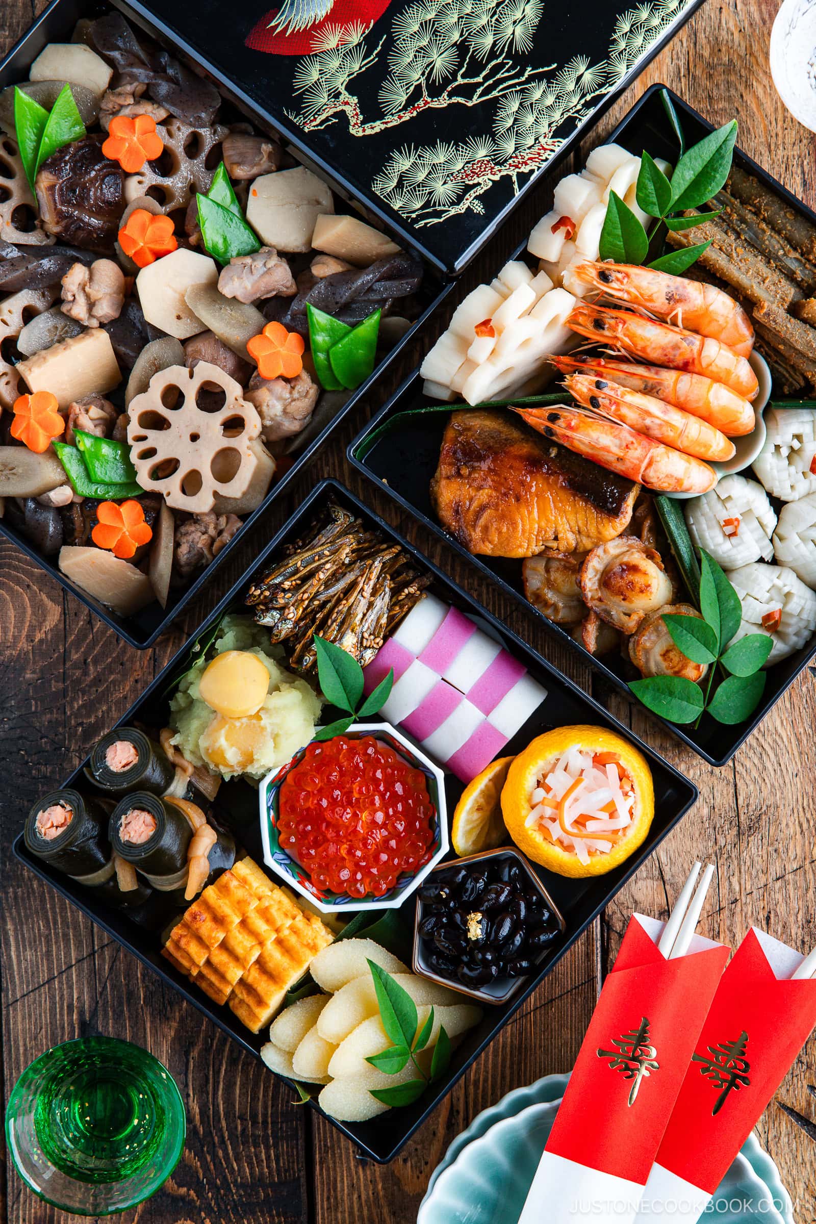 A traditional Japanese New Year’s feast (osechi ryori) in elegant black lacquer boxes, featuring assorted seafood, vegetables, rolled omelet, pickled dishes, and decorative garnishes, set on a wooden table with chopsticks.