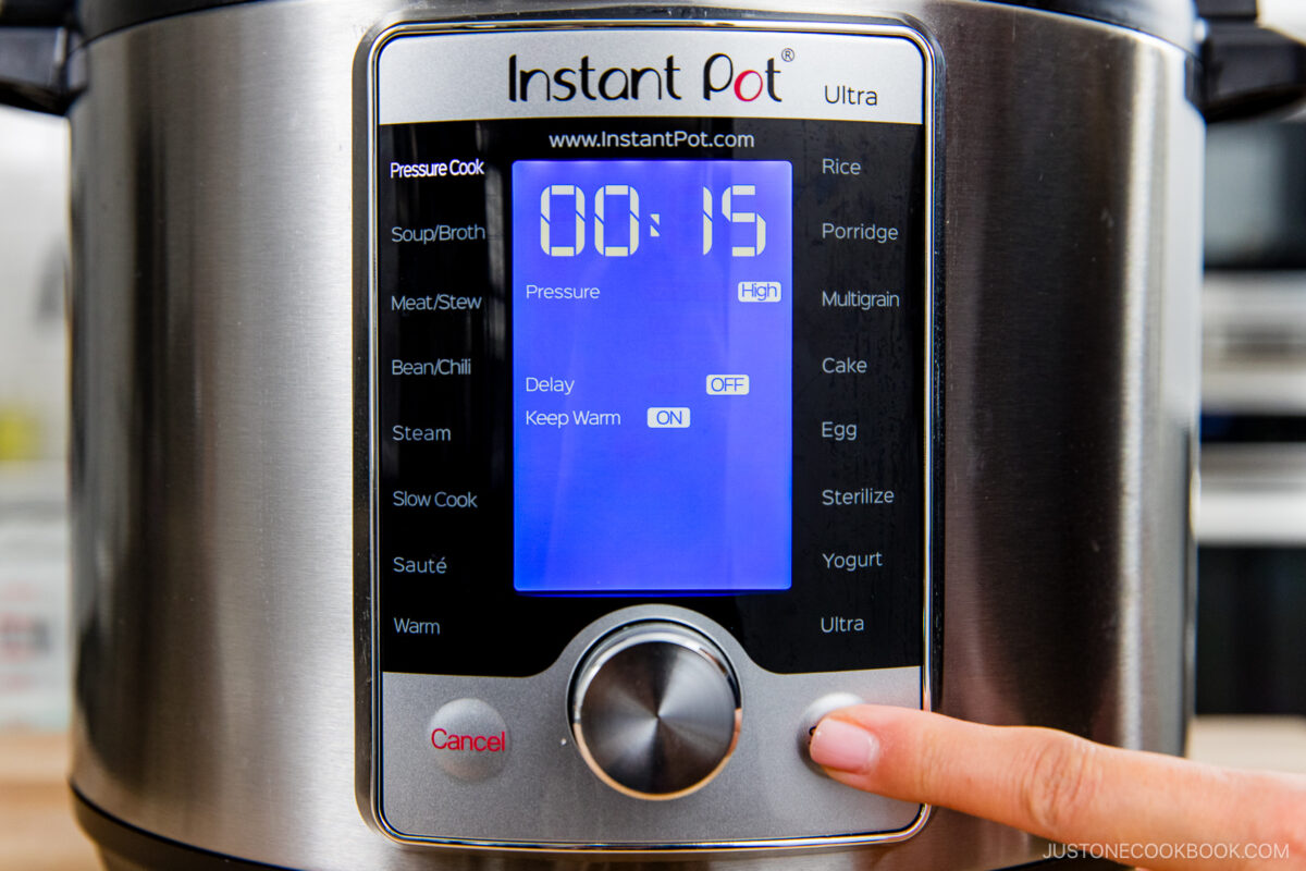 A close-up of an Instant Pot Ultra control panel with the timer set to 15 minutes. A person’s finger is pressing a button on the lower right side of the display.