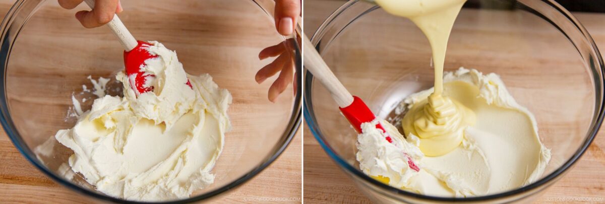 A close-up of hands using a red spatula to mix creamy white cheese in a glass bowl, then pouring thick yellow batter for matcha tiramisu over it on a wooden surface.