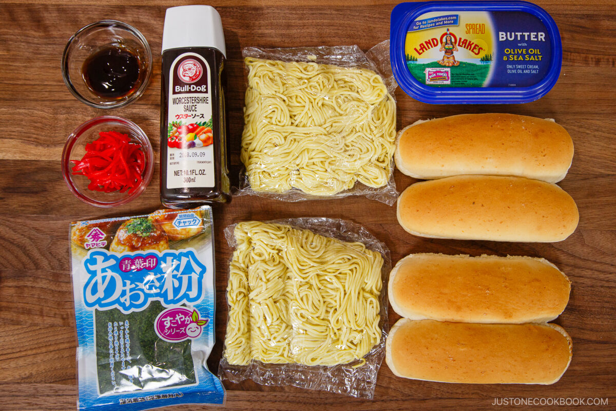 Ingredients for yakisoba pan laid out on a wooden surface: Bulldog sauce, yakisoba noodles, Land O’Lakes butter, four hot dog buns, aonori seaweed flakes, pickled ginger, and a small bowl of oyster sauce for that perfect yakisoba pan flavor.