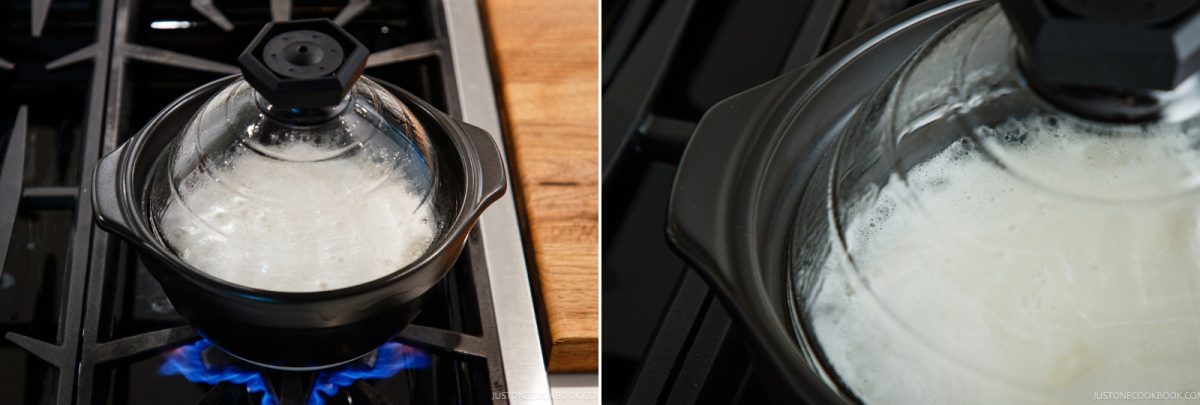 A black clay donabe with a clear glass lid containing boiling rice on a gas stove.