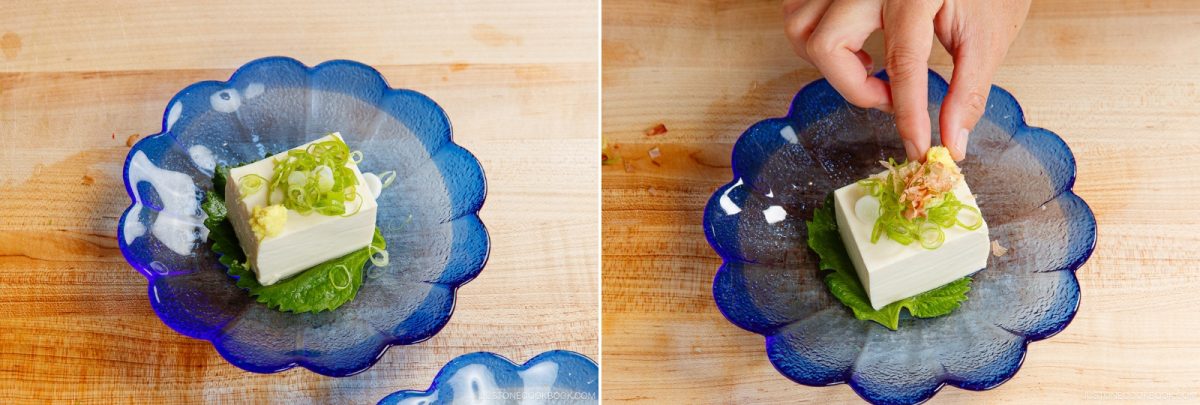 A block of tofu, prepared in the style of Hiyayakko (Japanese Cold Tofu), is topped with sliced green onions and grated ginger on a blue plate. In the second image, a hand adds more garnish to the refreshing Hiyayakko, enhancing its delicate presentation.