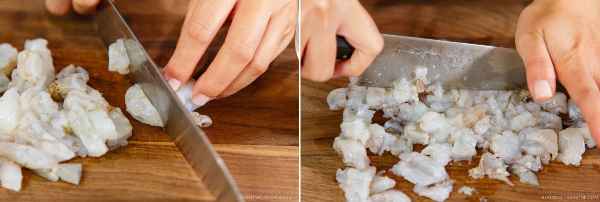 Close-up of hands finely chopping raw shrimp for Wonton Soup on a wooden cutting board with a large kitchen knife.