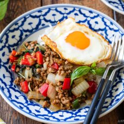 A plate of flavorful gapao rice topped with a perfectly fried egg and served with steaming white rice.
