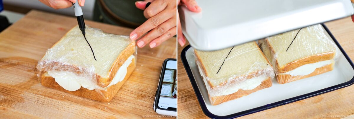 A person cuts through plastic-wrapped Japanese Fruit Sandwiches with a knife on a wooden board, then places a metal tray lid over two wrapped sandwiches in a white dish.