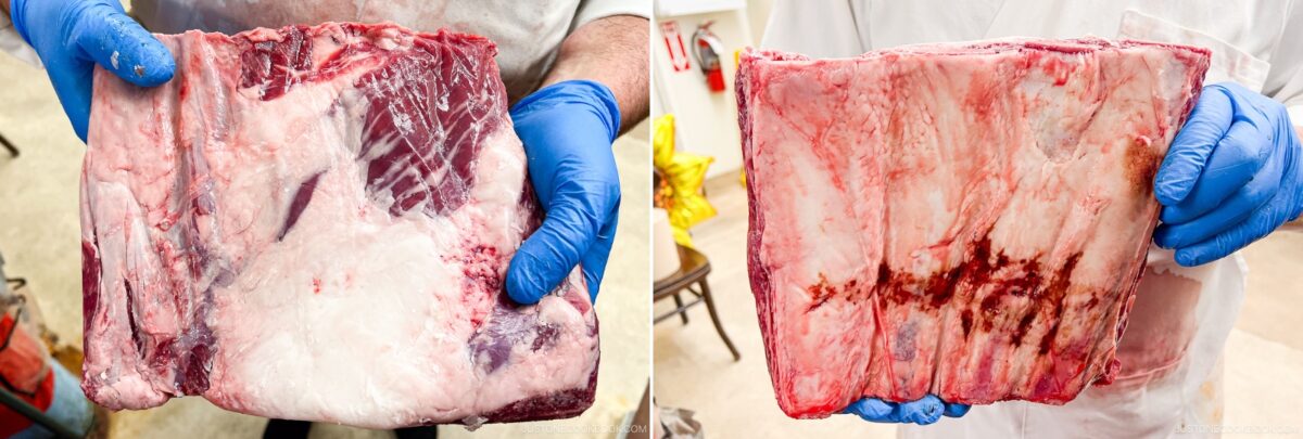 Two people wearing blue gloves and white coats each hold up large, raw cuts of beef, marbled with fat. The background appears to be a butcher shop where smoked beef ribs might soon be prepared.