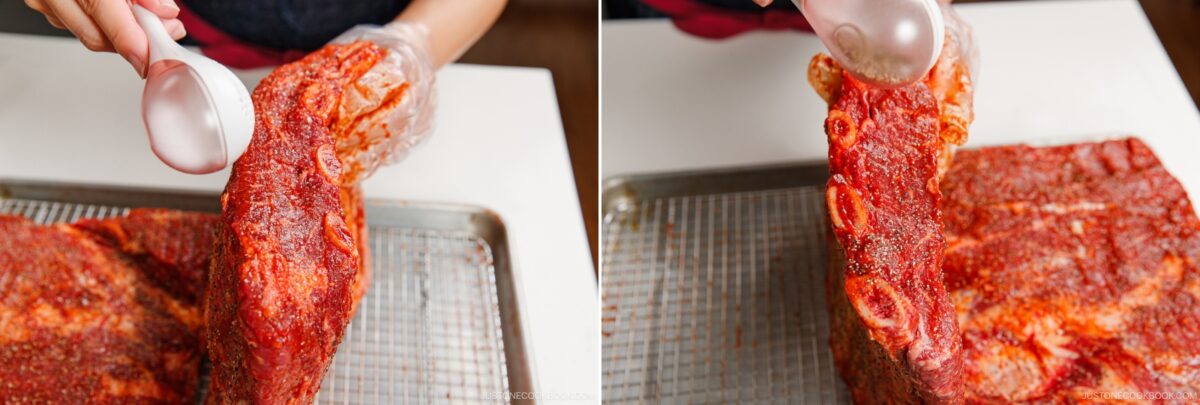 A person wearing gloves sprinkles seasoning onto a large slab of smoked beef ribs positioned on a wire rack over a baking sheet. The images are shown side by side, highlighting the process from different angles.