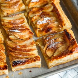 Easy Apple Tart: Rectangular slices of apple tart with flaky crust, topped with thinly sliced apples, cinnamon, and powdered sugar, arranged on a baking sheet lined with parchment paper.