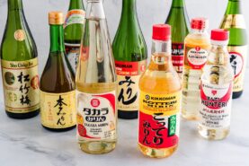Several bottles of Japanese cooking sake, mirin, and rice wine are grouped together on a light surface. Explore Sake vs Mirin: Key Differences and How to Use Them as shown by the colorful labels in Japanese and English.